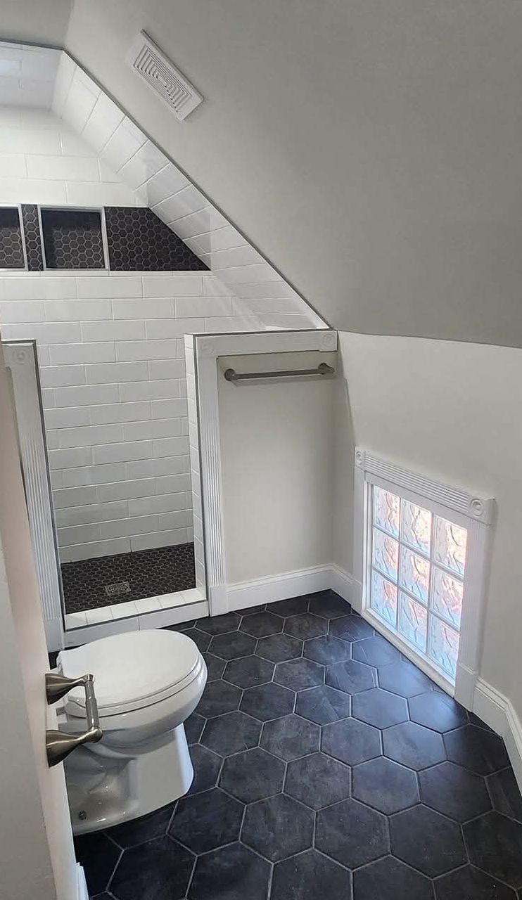 Finished attic bathroom with a tiled walk-in shower and black hex tile floor