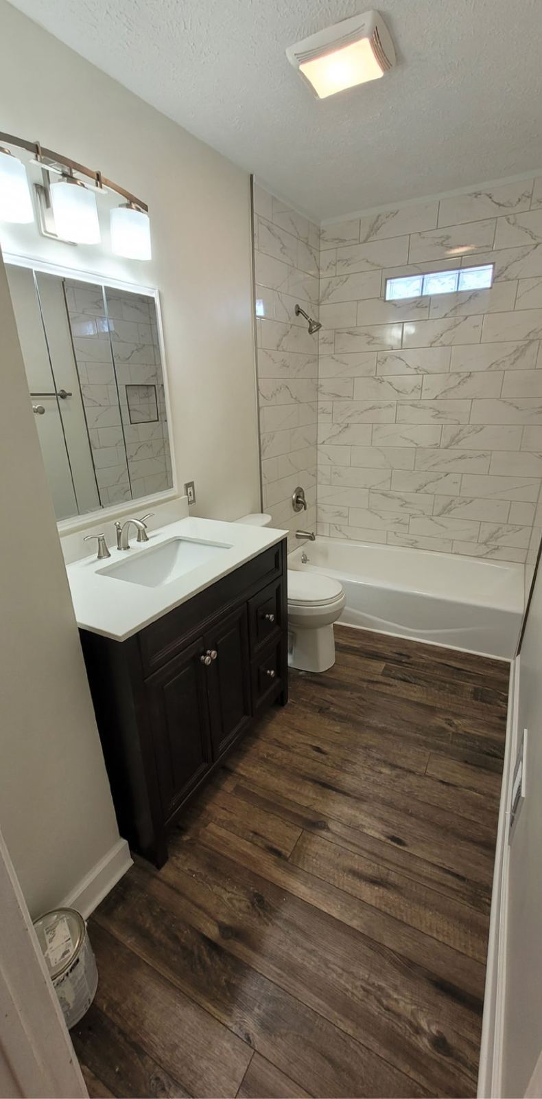 Remodeled bathroom with marble-look tile surround and a dark vanity