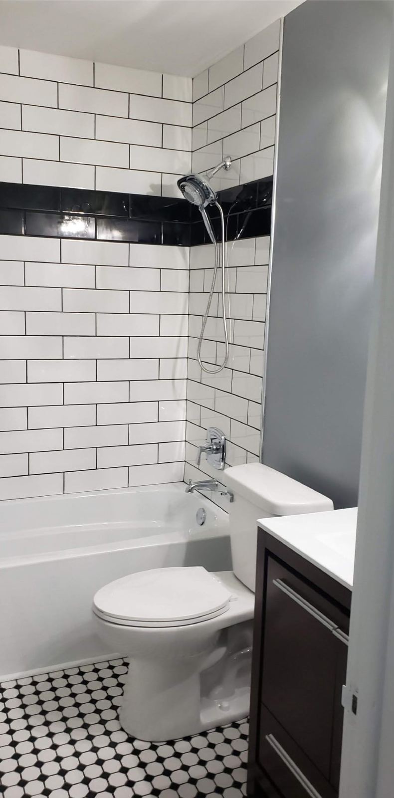 Remodeled bathroom with white subway tile, black accent band and hex tile floor