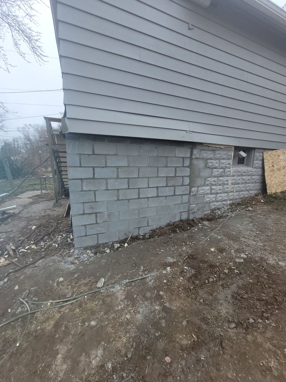 Rebuilt block foundation wall with siding and gutter reinstalled above